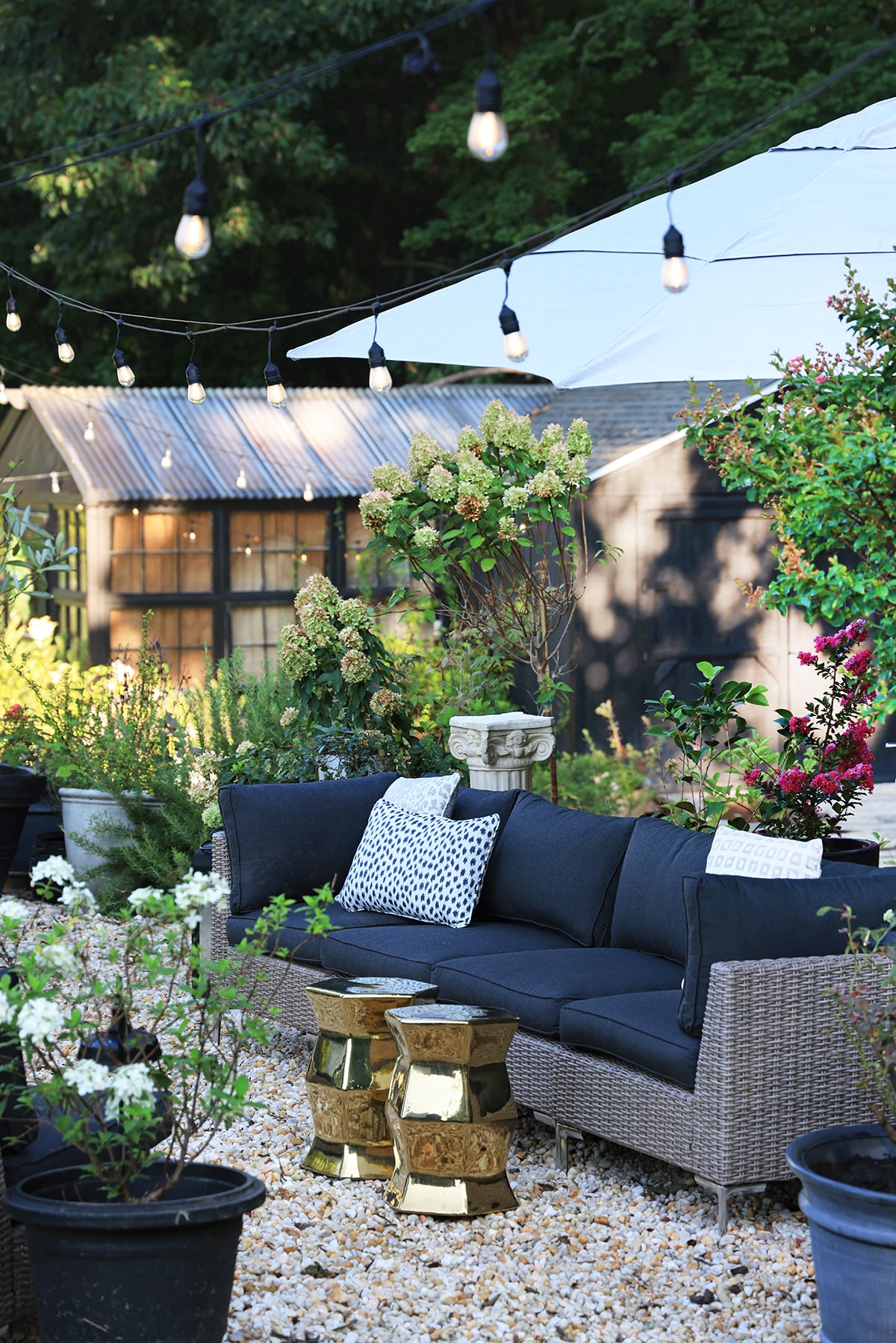 Outdoor sofa sectional set in a garden with string lights and gold garden stools